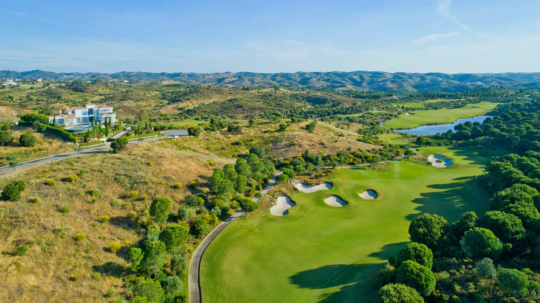 aerial view of a lush golf course with a grand mansion and rolling hills